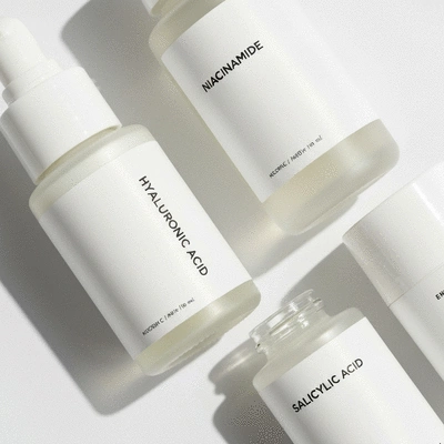 Close-up of three skincare product bottles with labels 'Hyaluronic Acid', 'Niacinamide', and 'Salicylic Acid' on a minimalist white background, no text, no words, no typography, clean image