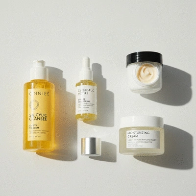 Flat lay of various skincare products, including serums, moisturizers, and cleansers, arranged neatly on a light-colored surface, emphasizing a complete skincare routine for dry, acne-prone skin. No text, no words, no typography, no labels, clean image.